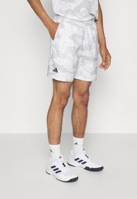 Vita sportshorts med ett subtilt grått abstrakt mönster. Elastisk midja och sidfickor. Matchas med vita sportskor och randiga strumpor.