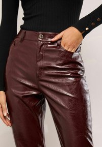 Burgundijas mākslīgās ādas bikses ar spīdīgu apdari, ar priekšējām kabatām un metalizētu pogu aizdari. Riblēts melns tops redzams attēla rāmī.