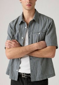 Short-sleeve checkered shirt in navy and white cotton, featuring a button-down collar and a front pocket with white stitching detail.