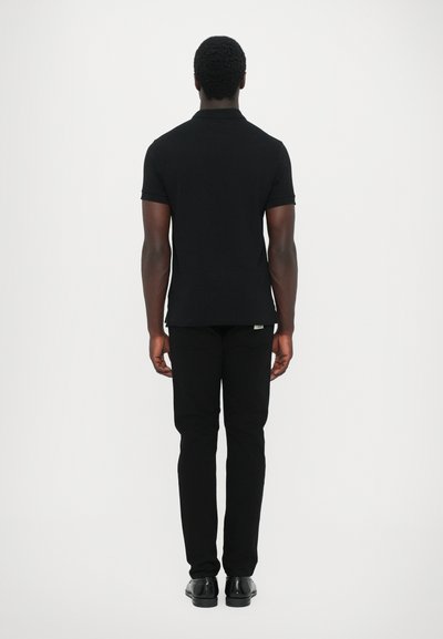 Black polo shirt with short sleeves, paired with black fitted pants. Smooth texture and clean design, viewed from the back.