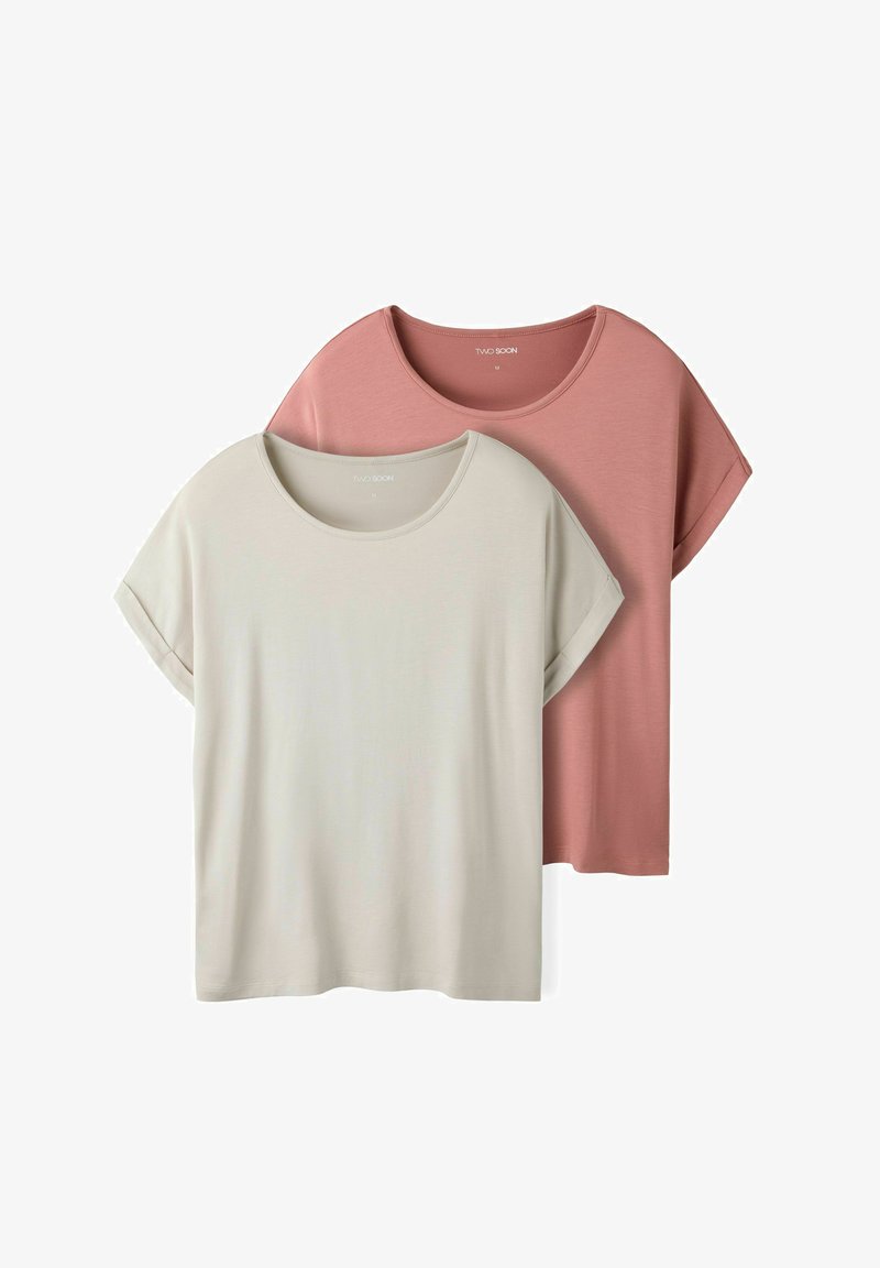 Deux t-shirts à manches courtes et col rond empilés ; le devant en beige clair, le dos en rose poudré, les deux avec des manches retroussées.