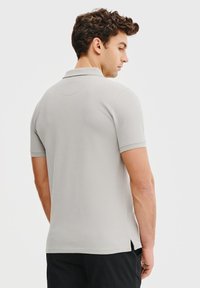 Jasnoszary polo z krótkim rękawem i kołnierzykiem. Posiada gładką fakturę oraz rozporki po bokach u dołu, co zapewnia swobodę ruchów.