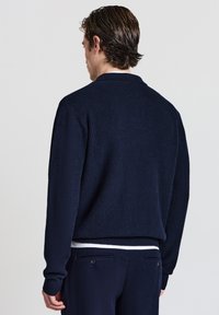 Marineblaues geripptes Sweatshirt mit lockerer Passform, das einen Kragen und lange Ärmel hat. Der Stoff hat eine strukturierte Oberfläche. Rückansicht dargestellt.