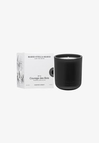 Candela profumata in vetro nero con finitura opaca, etichettata "Courage des Bois", in una scatola bianca che mostra i dettagli del prodotto. Peso 300g.
