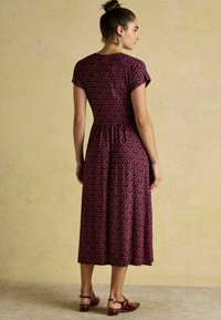 Ärmelloses knielanges Kleid in dunklem Merlot mit floralen Mustern in Pink und Blau. Der Stoff wirkt weich und hat eine leicht geraffte Taille.