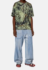 Tričko s krátkým rukávem, zeleno-hnědý vzor, volný střih, doplněné světle modrými oversized džínami a červenými sportovními botami.