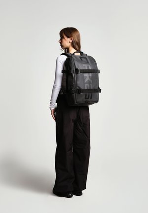 Zaino nero con spallacci regolabili e fibbie laterali, realizzato in materiale resistente. Presenta un grande logo e una forma rettangolare.