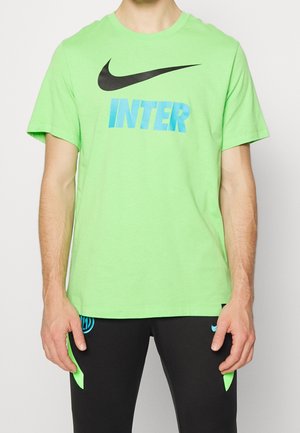Man wearing a bright green Nike T-shirt with black swoosh and blue "INTER" text, paired with black pants featuring green and blue accents.