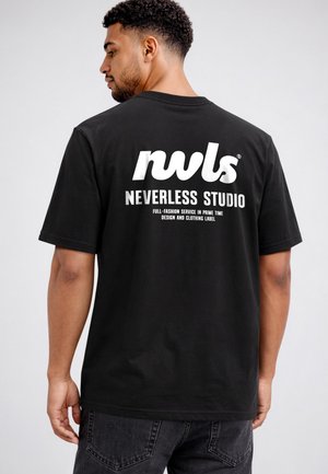 Mann mit kurzen lockigen Haaren, der ein schwarzes T-Shirt mit weißem Text "nwls Neverless Studio" und zusätzlichem kleinem Text auf dem Rücken trägt.