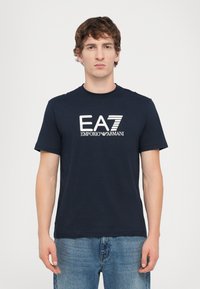 T-shirt in cotone blu navy con maniche corte, caratterizzato da un logo ricamato EA7 Emporio Armani in bianco sul petto.