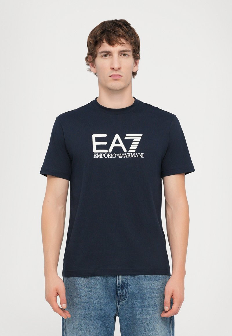 T-shirt in cotone blu navy con maniche corte, caratterizzato da un logo ricamato EA7 Emporio Armani in bianco sul petto.