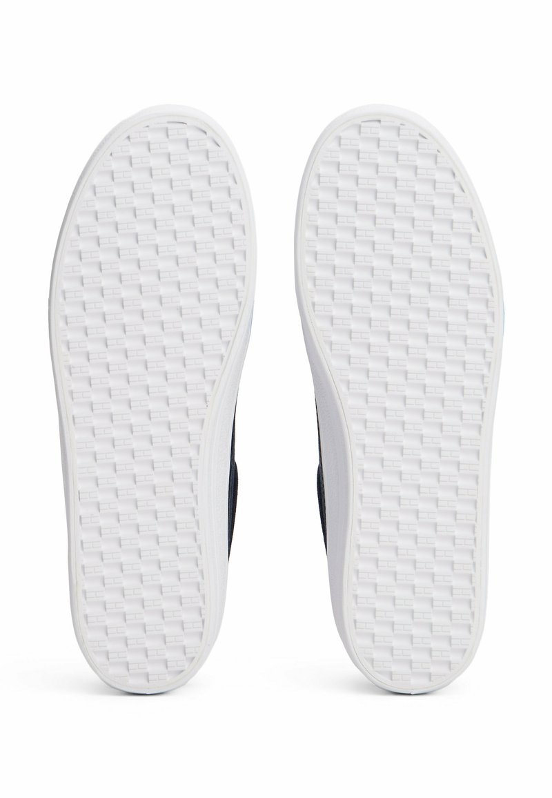 Semelles de chaussures avec une base en caoutchouc blanc, texturées avec un motif tissé. Les côtés sont d'un bleu marine foncé, offrant une couleur contrastante par rapport à la semelle.