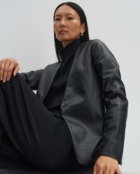 Schwarze Lederblazer mit einem einzigen Knopfverschluss, leicht taillierter Passform und glatter Textur, kombiniert mit einem schwarzen Rollkragenpullover.