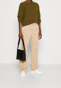 Zelenohnědý, ribbovaný svetr; béžové, rovné kalhoty; černá, texturovaná kabelka; bílé tenisky. Jednoduchý, neformální outfit.