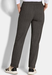 Donker houndstooth gemusterde broeken met een rechte pasvorm, elastische tailleband en omgeslagen broekspijpen, gecombineerd met beige en zwarte sneakers.