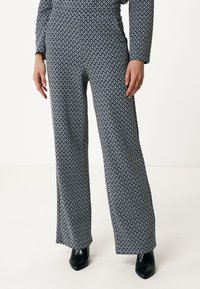 Wijde broek in marineblauwe stof met een geometrisch wit patroon. Zachte textuur met een hoge tailleband en gecombineerd met zwarte hakken.