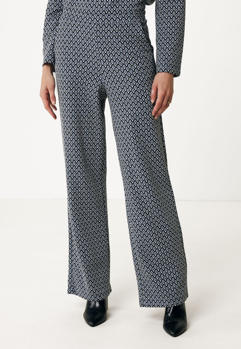 Wijde broek in marineblauwe stof met een geometrisch wit patroon. Zachte textuur met een hoge tailleband en gecombineerd met zwarte hakken.