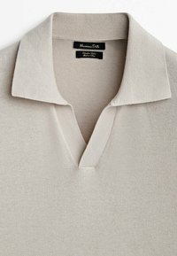 Polo en tricot beige avec un col en V, un col texturé et des manches courtes. Étiquette visible avec la marque "Massimo Dutti".