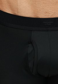 Κοντινό πλάνο στο κάτω μέρος του κορμού ενός άνδρα που φοράει μαύρα ανδρικά εσώρουχα Abercrombie & Fitch με ελαστική μέση και μπροστινή περιφερειακή θήκη.