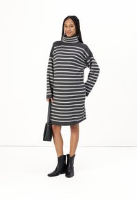 Robe en col roulé gris charbon avec des rayures horizontales grises ; coupe ample avec des manches longues et un détail sur le côté ; associée à des bottines noires.
