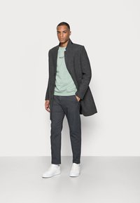 Mørkegrå uldfrakke med krave, parret med en lys grøn sweatshirt, grå bukser og hvide sneakers. Enkel, skræddersyet design.