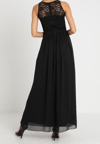 Svart maxiklänning med spetsöverdel och plisserad kjol. Har hög halsringning, dragkedja i ryggen och genomskinlig tyg längst ner med en svävande silhuett.