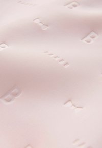 Jasnoróżowa tkanina z wytłaczanym wzorem liter i kokardek. Gładka faktura z subtelnym połyskiem, tworząca miękki wygląd.