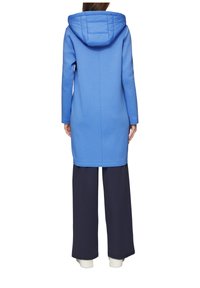 Felpa lunga blu con cappuccio imbottito, tessuto morbido, tasche laterali e taglio dritto, abbinata a pantaloni ampi neri.