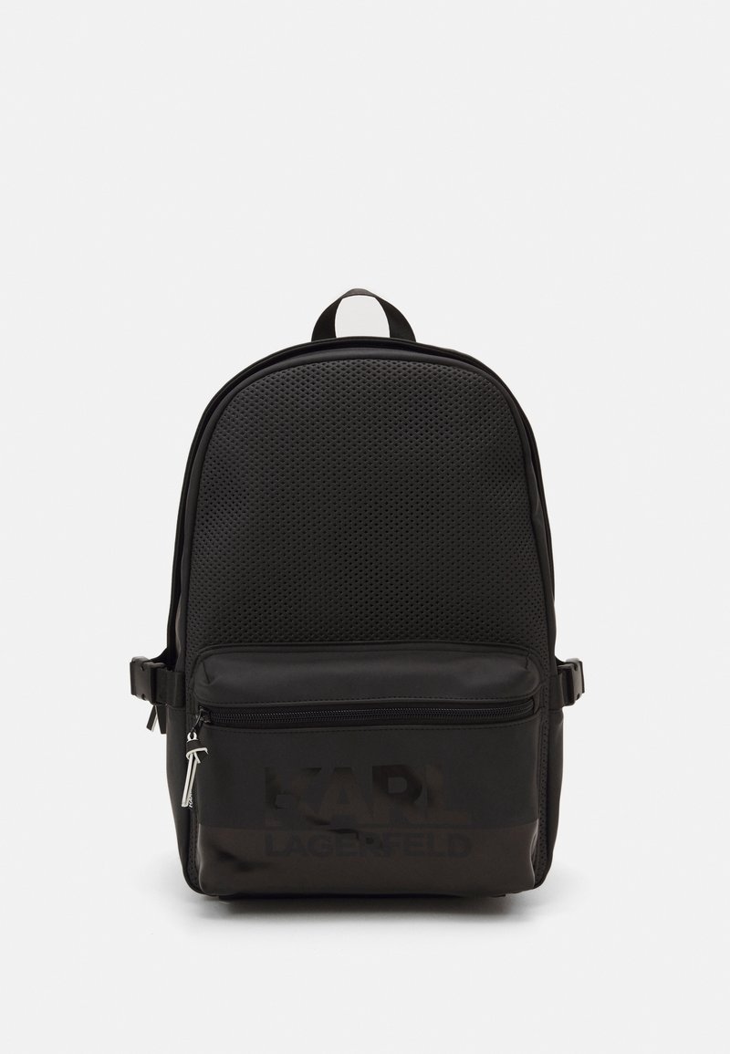 Schwarzer Rucksack mit einer strukturierten, durchlöcherten Oberfläche. Verfügt über eine Reißverschlusstasche auf der Vorderseite und ein Logo-Detail am Boden. Mit verstellbaren Trägern.