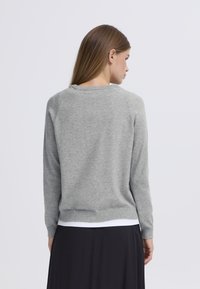 Svetlosiv pleteni pulover z okroglim izrezom, dolgimi rokavi in rebrastim robom. Pogled od zadaj prikazuje mehak teksturo in brezšivno obliko.