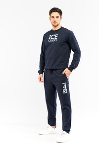 Marine sweatshirt og matchende joggers lavet af blødt stof, med hvid "ICE"-logo tryk og sidelommer, parret med hvide sneakers.