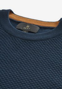 Pull en maille bleu marine avec un motif texturé et un col côtelé orange. Comprend une étiquette avec "NEXT" et la taille "M".
