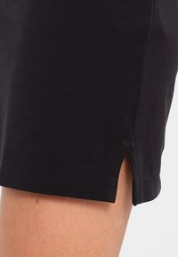 Jupe en coton noir avec une finition texturée, dotée de fentes sur les côtés pour faciliter les mouvements. Design simple sans accents visibles.