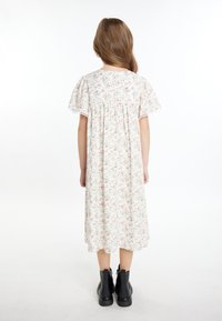 Floral jurk met korte, gerimpelde mouwen, een lichte achtergrond en kleine roze en groene patronen, gecombineerd met zwarte enkellaarsjes.