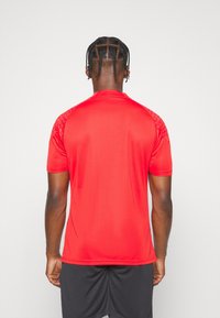 Maglietta sportiva rossa a maniche corte con una texture liscia, con dettagli a motivo sulle spalle, vista da dietro.