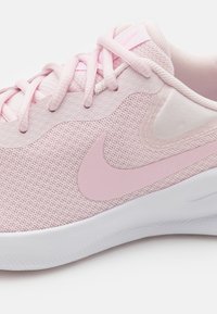 Light pink sneaker with mesh upper, soft texture, flat laces, and a prominent pink Nike swoosh. White sole with subtle texture detail.