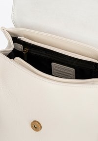 Bílá kožená kabelka s zdrsněnou texturou, která má magnetické zapínání, zipovou kapsu a šedou látkovou podšívku. Interiér má více přihrádek.