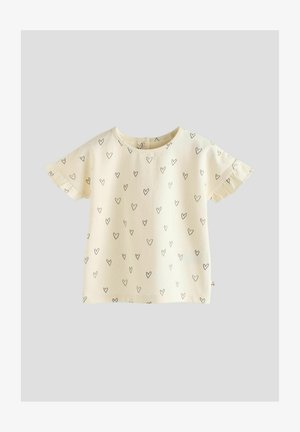 Light yellow short-sleeve top with scattered black heart print, rounded neckline, and ruffled sleeve edges. Soft cotton material.