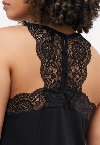 Schwarz Oberteil mit Spitzenrücken und floralen Mustern, Knopfdetails und einem glatten Stoffkörper. Die Spitze reicht bis zum Ausschnitt für einen zusätzlichen Akzent.