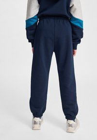 Mörkblå träningsbyxor med elastisk midja och avsmalnande avslut, tillverkade av mjukt material. I kombination med ljusa sneakers.