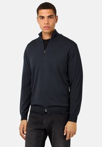 Moška zadrgo zapirana cardigan v temno modri barvi. Pletenina, klasičen kroj, rebrasti manšeti in rob. Zadrga s visokim ovratnikom. Priložnostna zasnova.