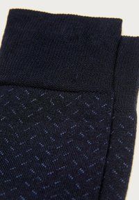 Un par de calcetines azul oscuro con sutiles patrones en zigzag y puños acanalados sobre un fondo claro.