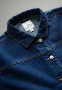 Jachetă din denim albastru închis cu guler, cusături vizibile, nasturi metalici tip capse și etichetă cu inscripția "THE SET", mărimea medie.