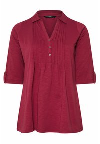 Blusa rossa da donna con maniche a 3/4, abbottonatura frontale, colletto e pieghe verticali sul petto.