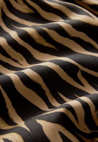 Tela texturizada con un patrón de rayas de cebra en negro y beige. El diseño es dinámico, con anchos de raya variables y una superficie suave.