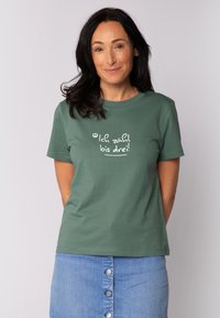 Grünes Baumwoll-T-Shirt mit rundem Halsausschnitt und kurzen Ärmeln. Auf der Vorderseite steht in verspielter Schrift "Ich zähl bis drei!" in weißer Farbe.