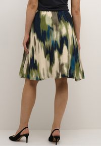 Une jupe A-line longueur genou avec un motif abstrait multicolore, présentant des teintes de vert, de bleu et de beige, fabriquée en tissu léger.