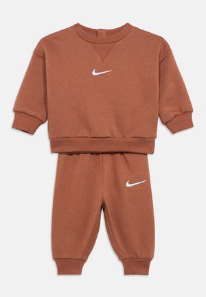 Chándal marrón para niños de dos piezas con mangas largas y pantalones, con logotipos blancos de Nike en forma de swoosh en el pecho y la pierna izquierda.