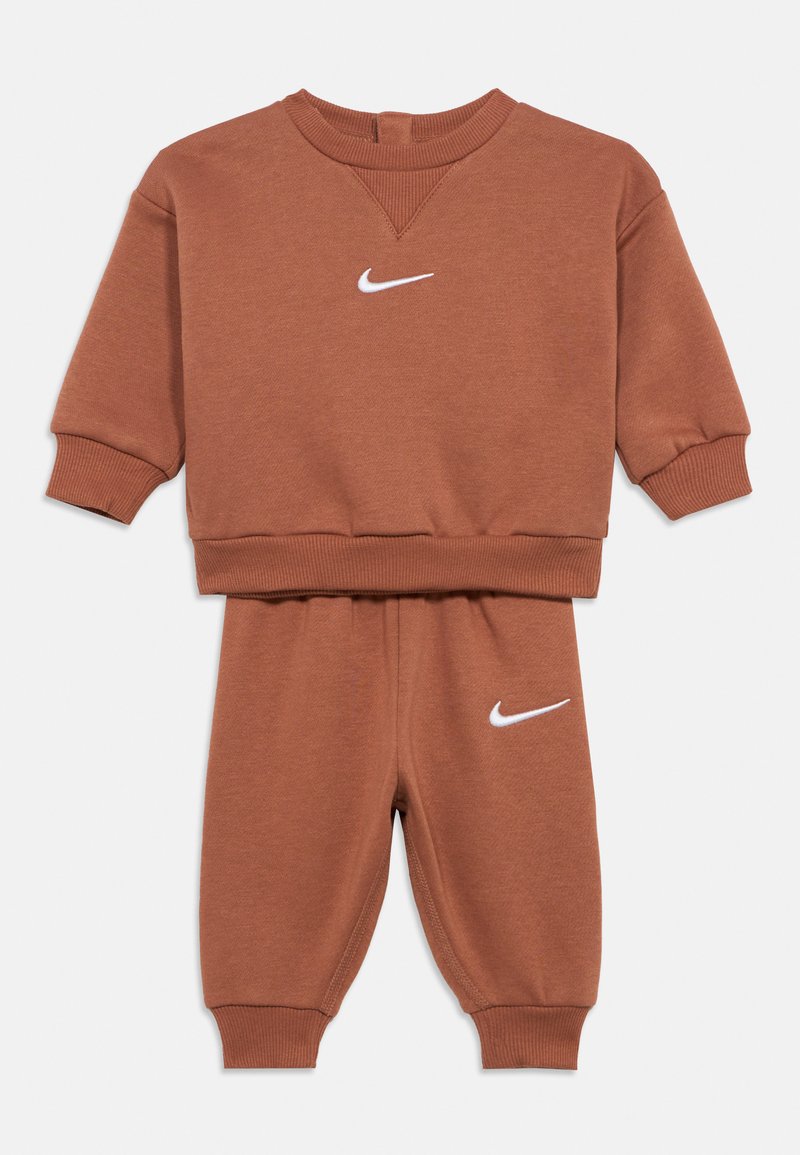 Chándal marrón para niños de dos piezas con mangas largas y pantalones, con logotipos blancos de Nike en forma de swoosh en el pecho y la pierna izquierda.
