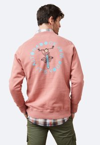 Sudadera de color rosa claro con un gráfico de una bicicleta en la parte posterior, con texto azul que dice "ALTONADOCK AVM IT'S YOUR." Puños y dobladillo de canalé.